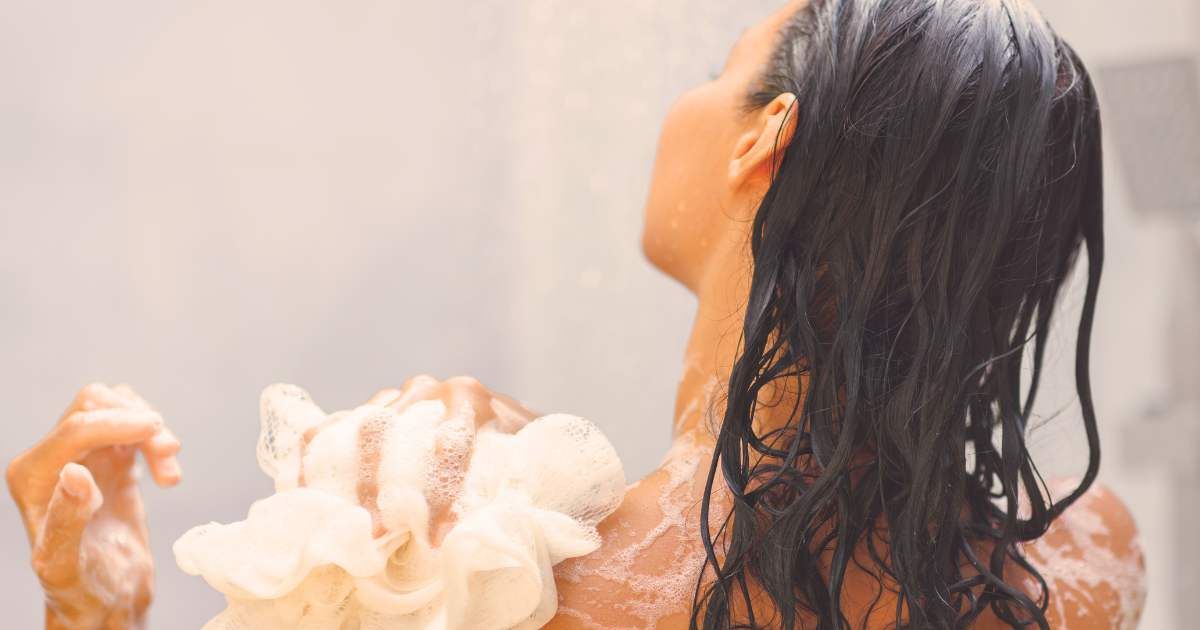 A woman with wet hair enjoys a refreshing shower while scrubbing her back with a foamy loofah. (Representative Cover Image Source: Getty | Dmytro Buianskyi)