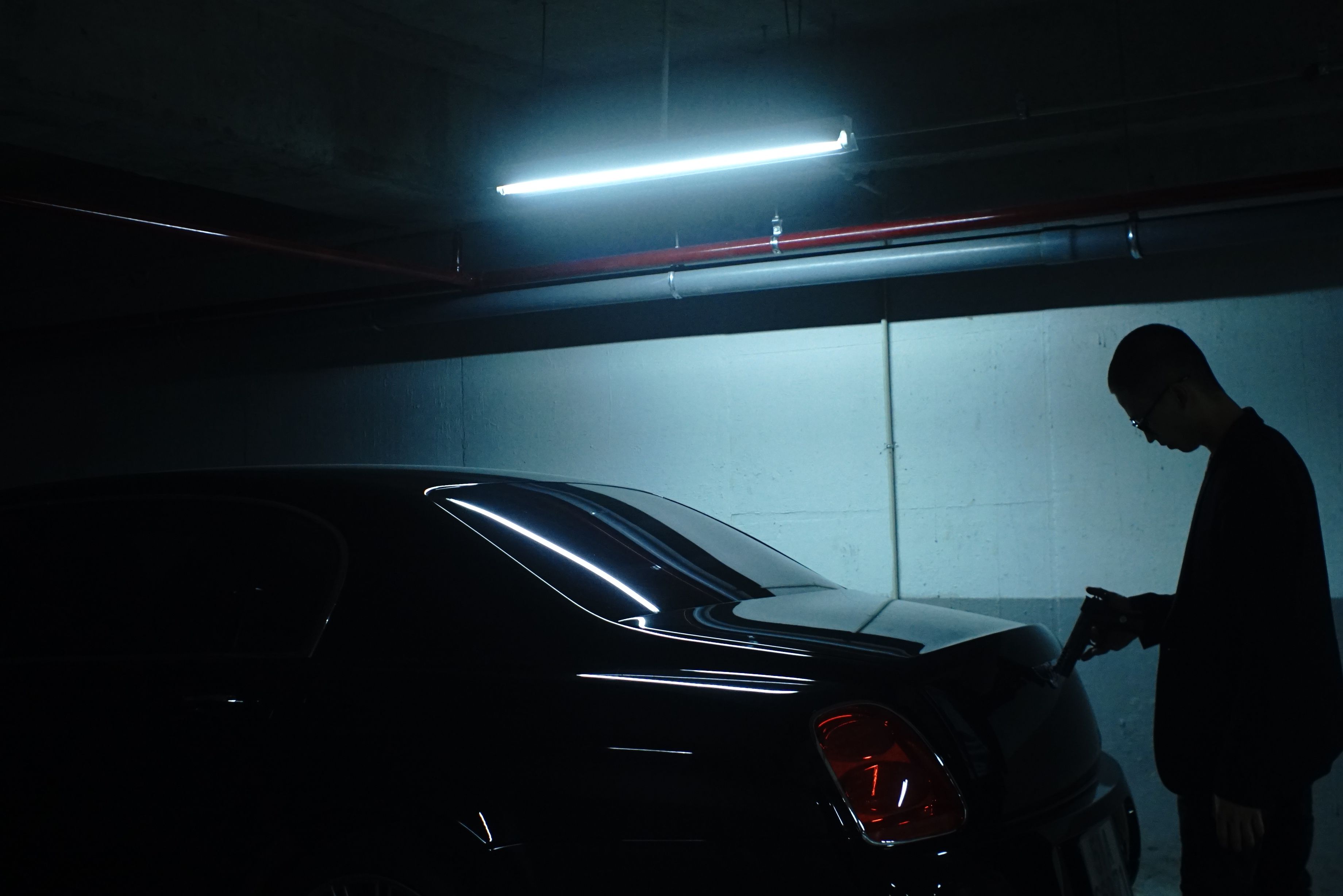 An armed man stands slyly behind a car.
