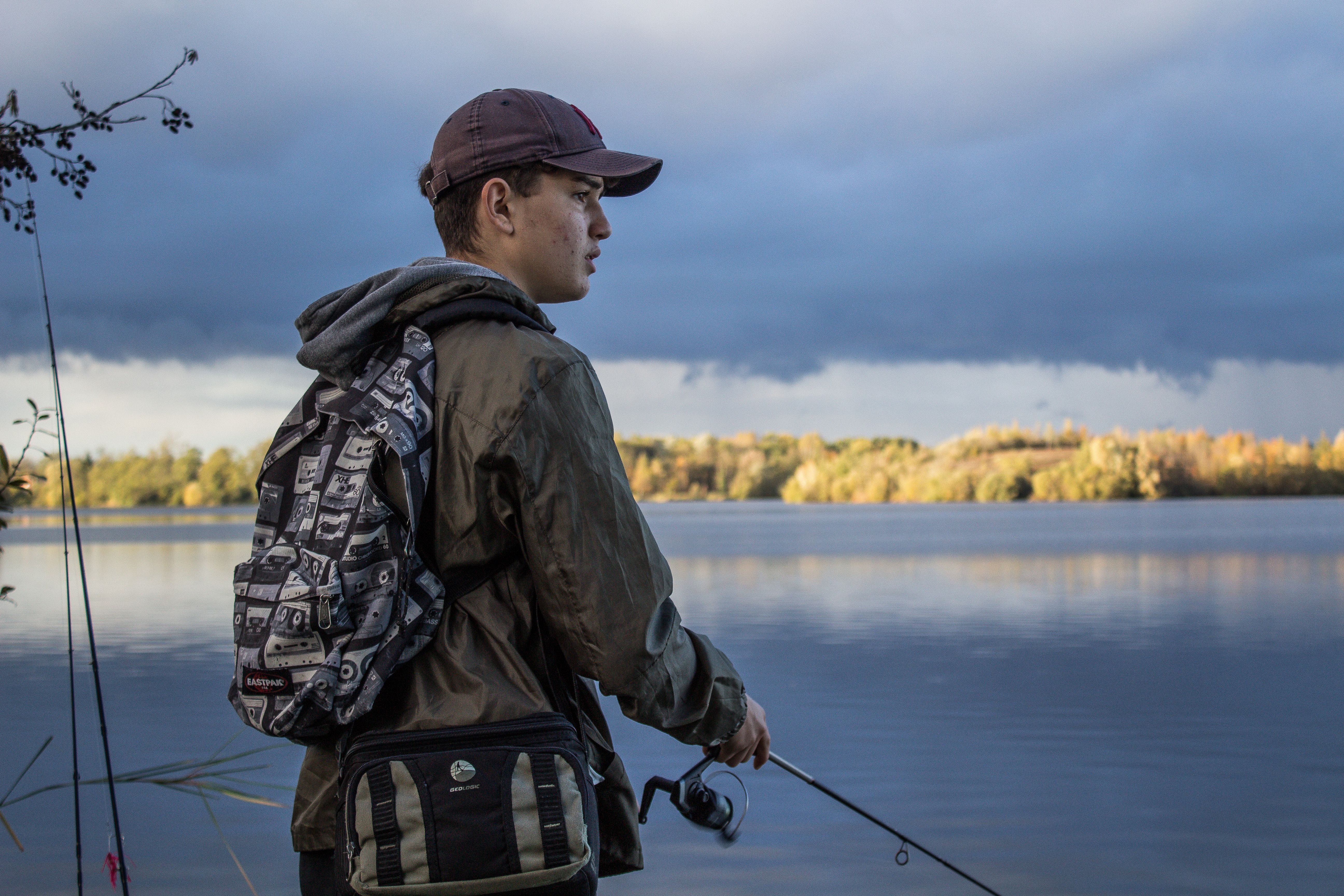 A teenage boy is near a lake, looking at something.