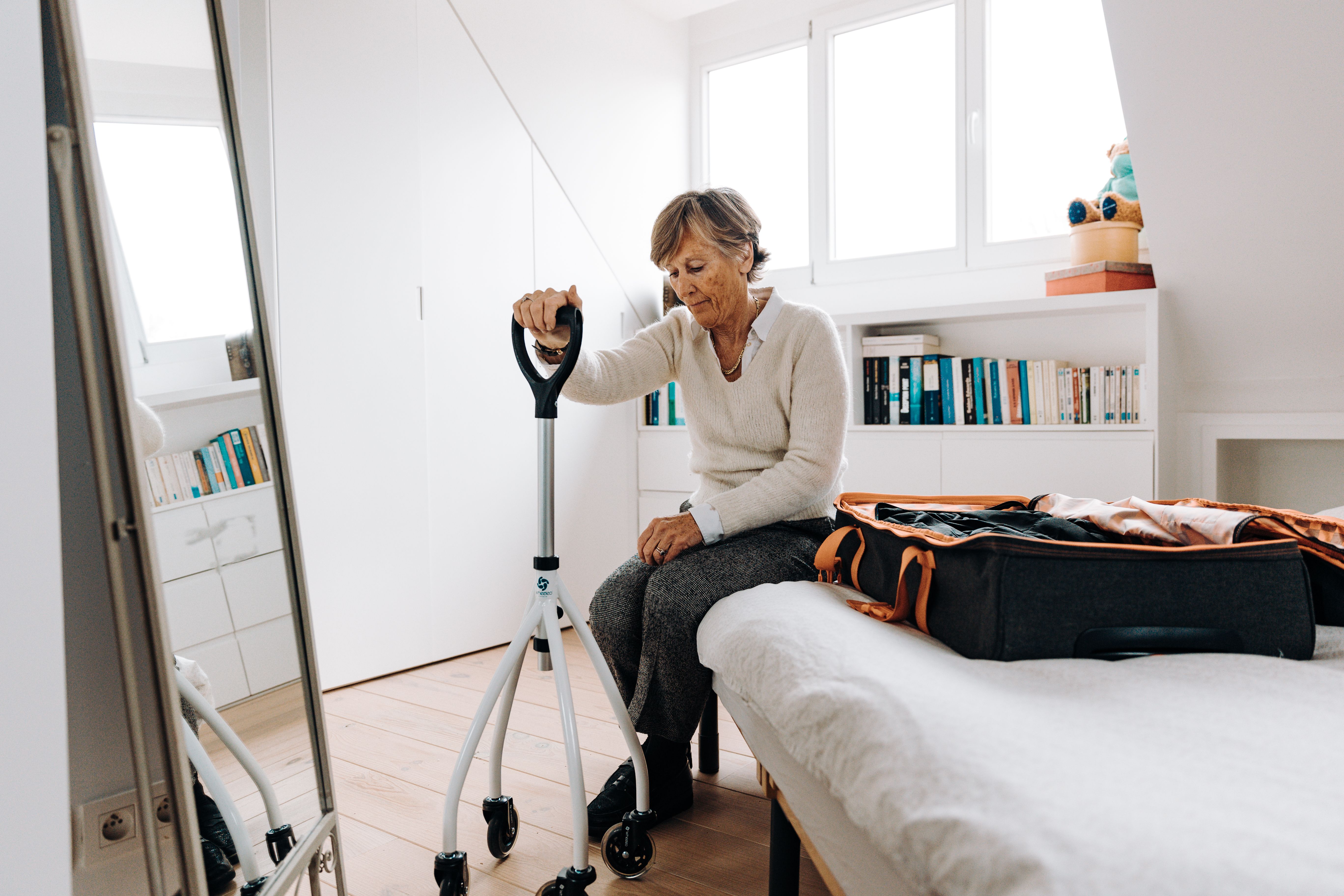 An elderly woman looks tired as she sits while holding onto walker.