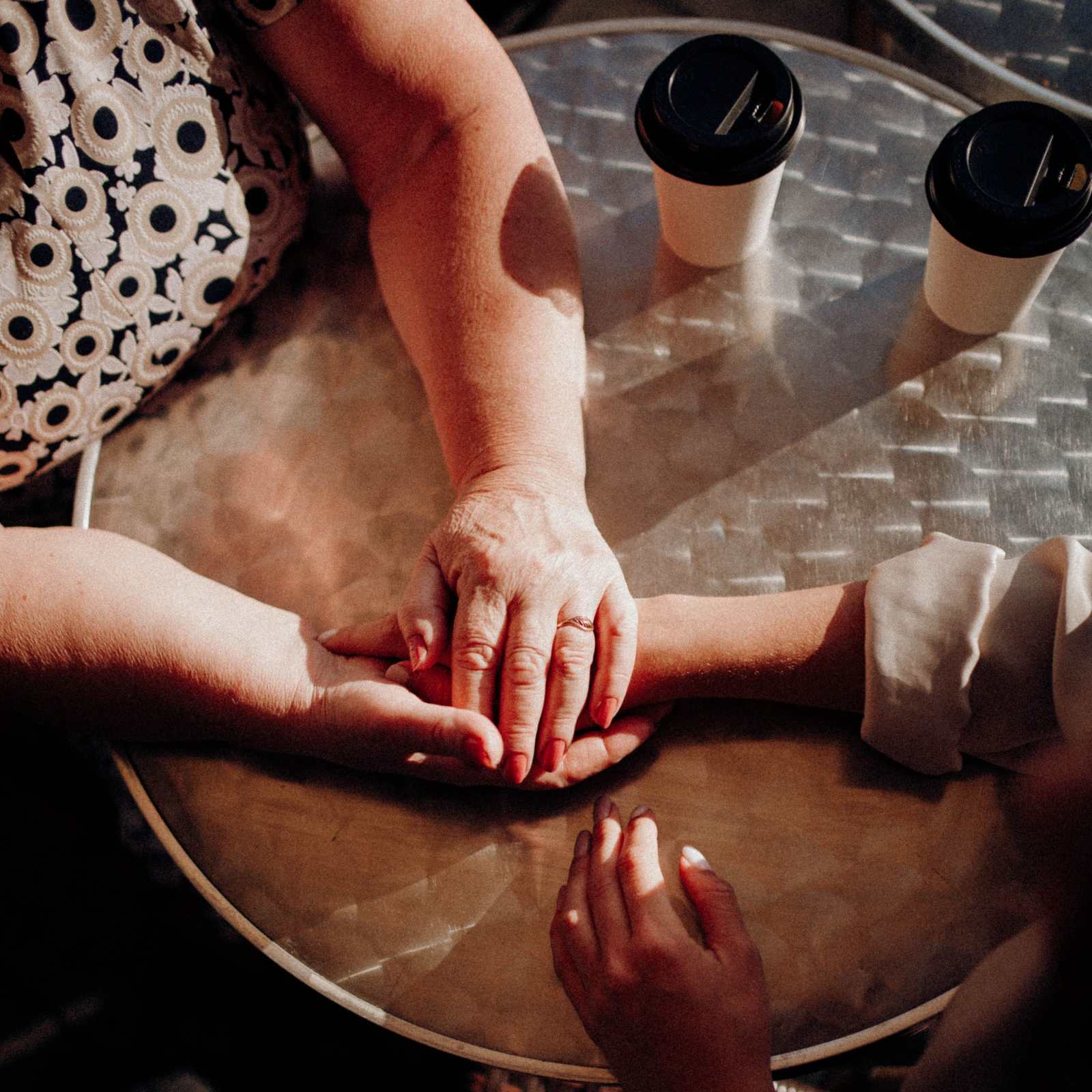 Two women sharing a heartfelt moment, holding hands over coffee. (Representative Image Source: Danik Prihodko)