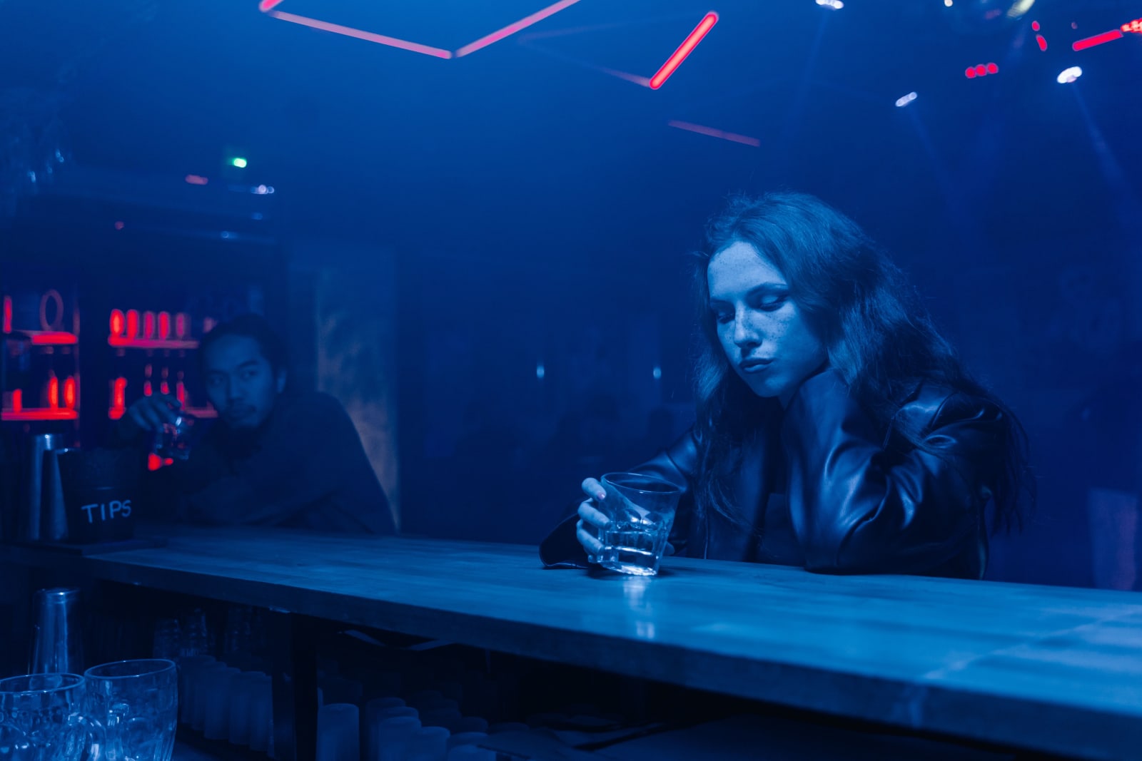A woman feeling sick at a bar while a man stares at her.