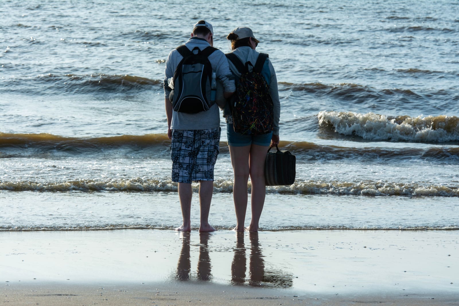 A couple is looking intently while standing at the beach shore.