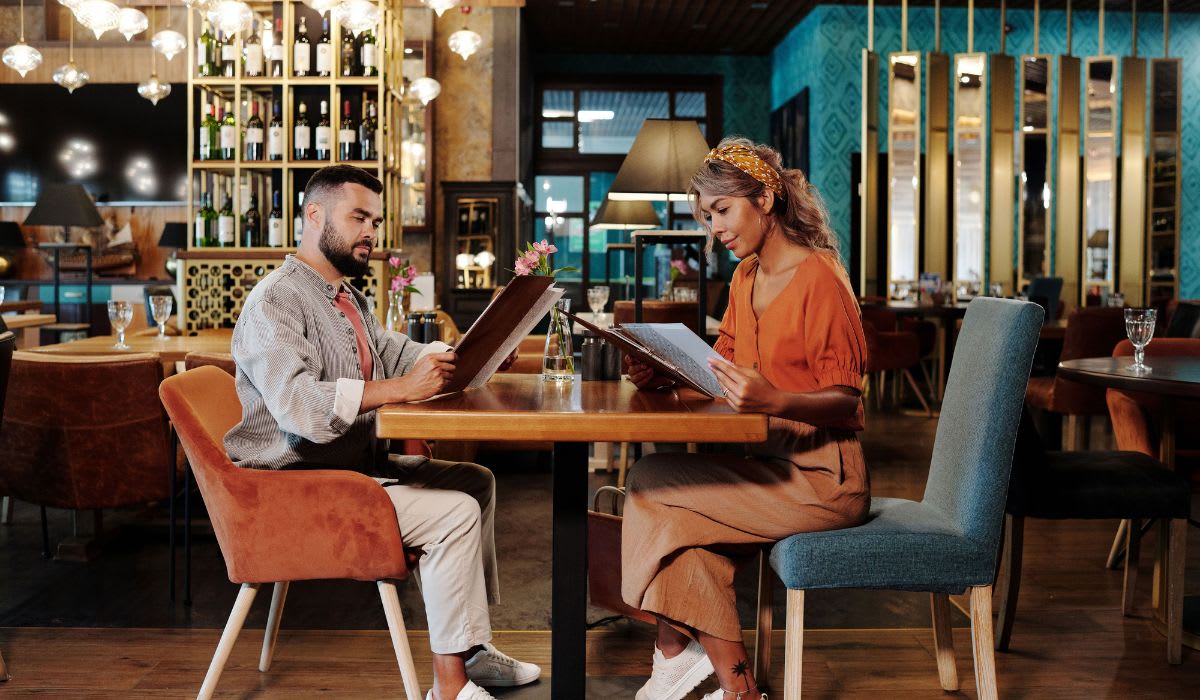 Couple sitting together at a stylish restaurant reviewing the menu. (Representative Image Source: Pexels | Jep Gambardella)