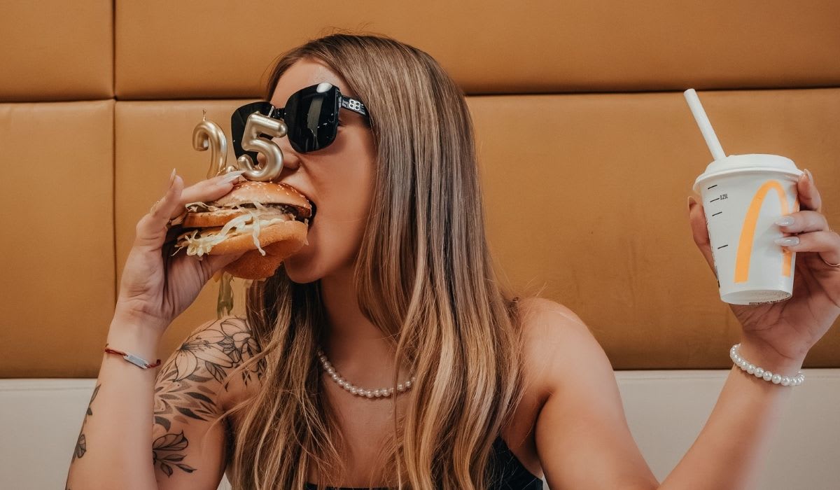 Woman in a casual outfit enjoying a burger. (Representative Image Source: Pexels | Karol Tomsia)