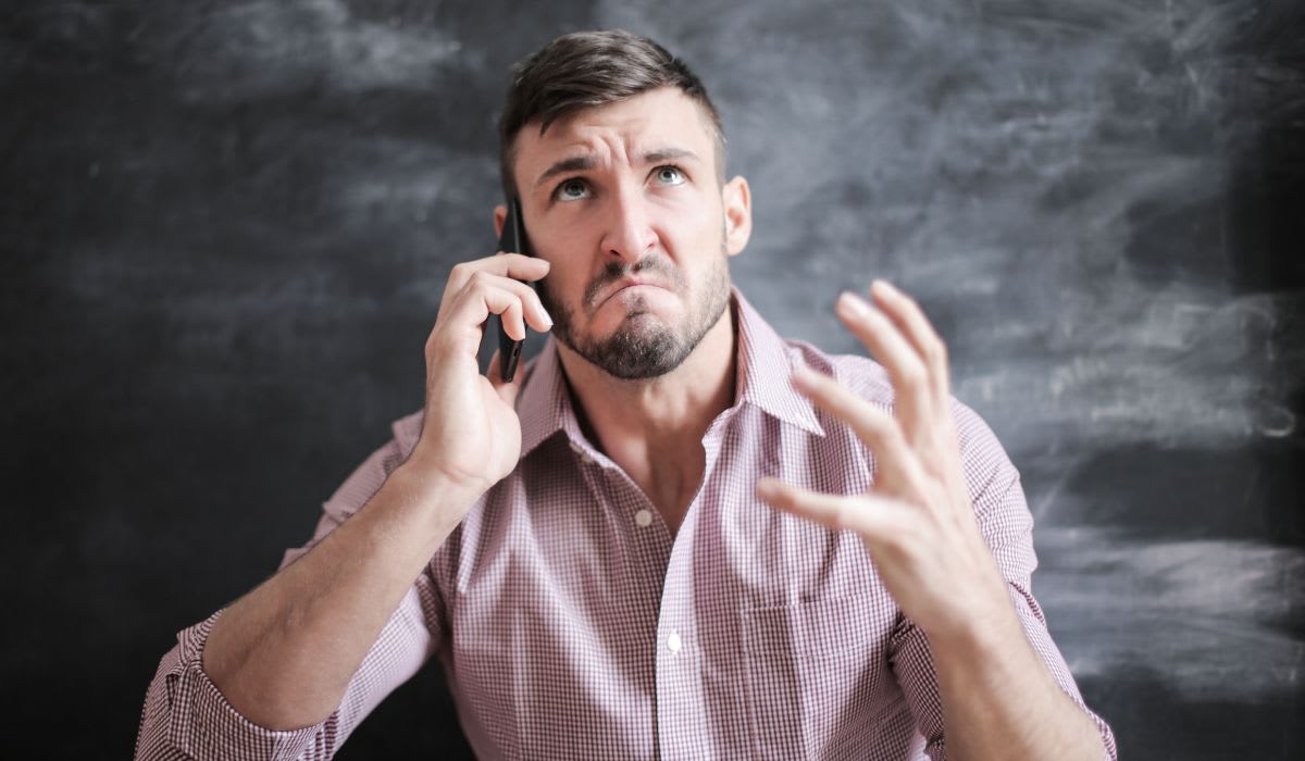 Man in pink dress shirt looking stressed while talking on a smartphone. (Representative Image Source: Pexels | Andrea Piacquadio)