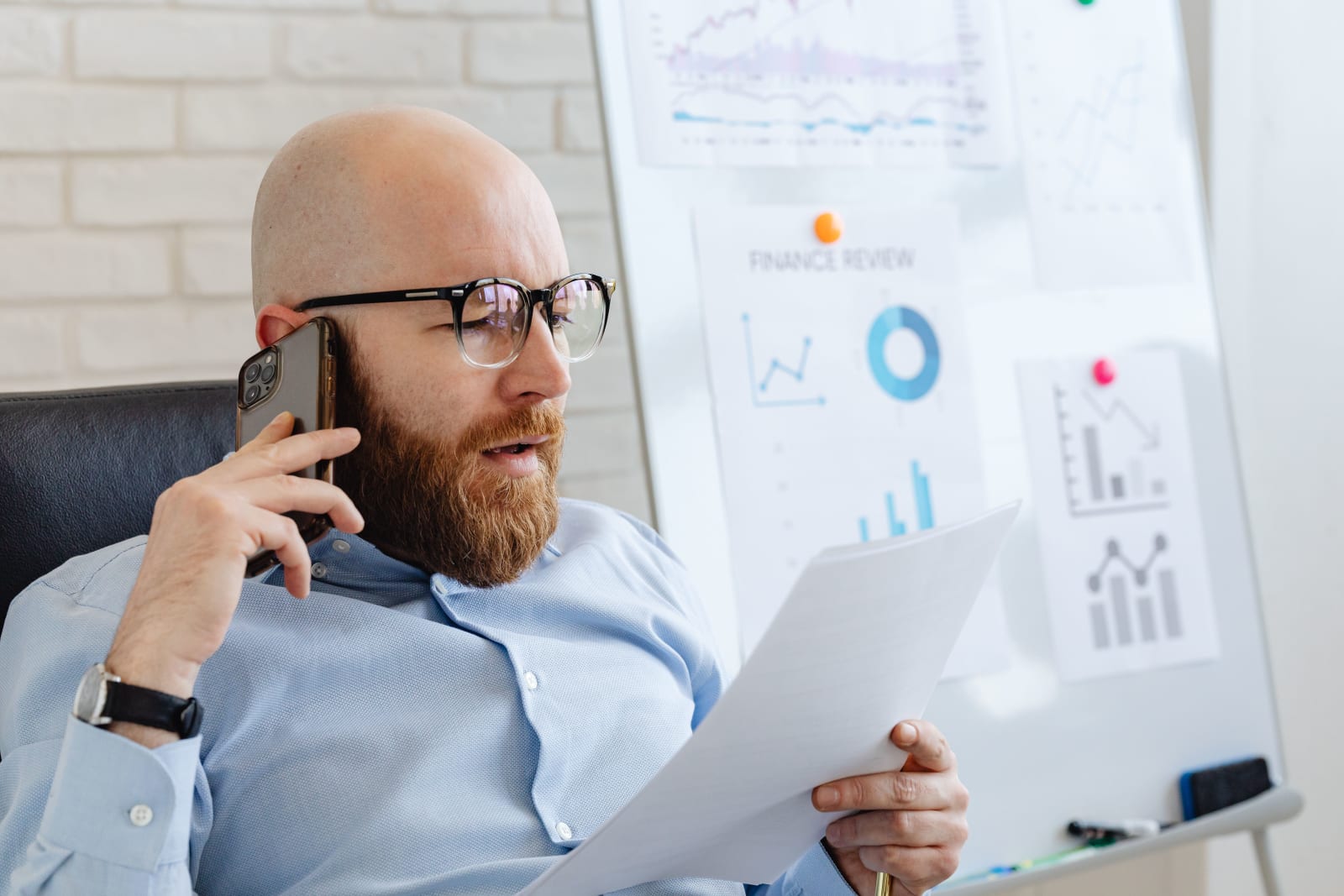 A manager speaking on the call while checking documents. (Representative Image Source: Pexels| Karola G)