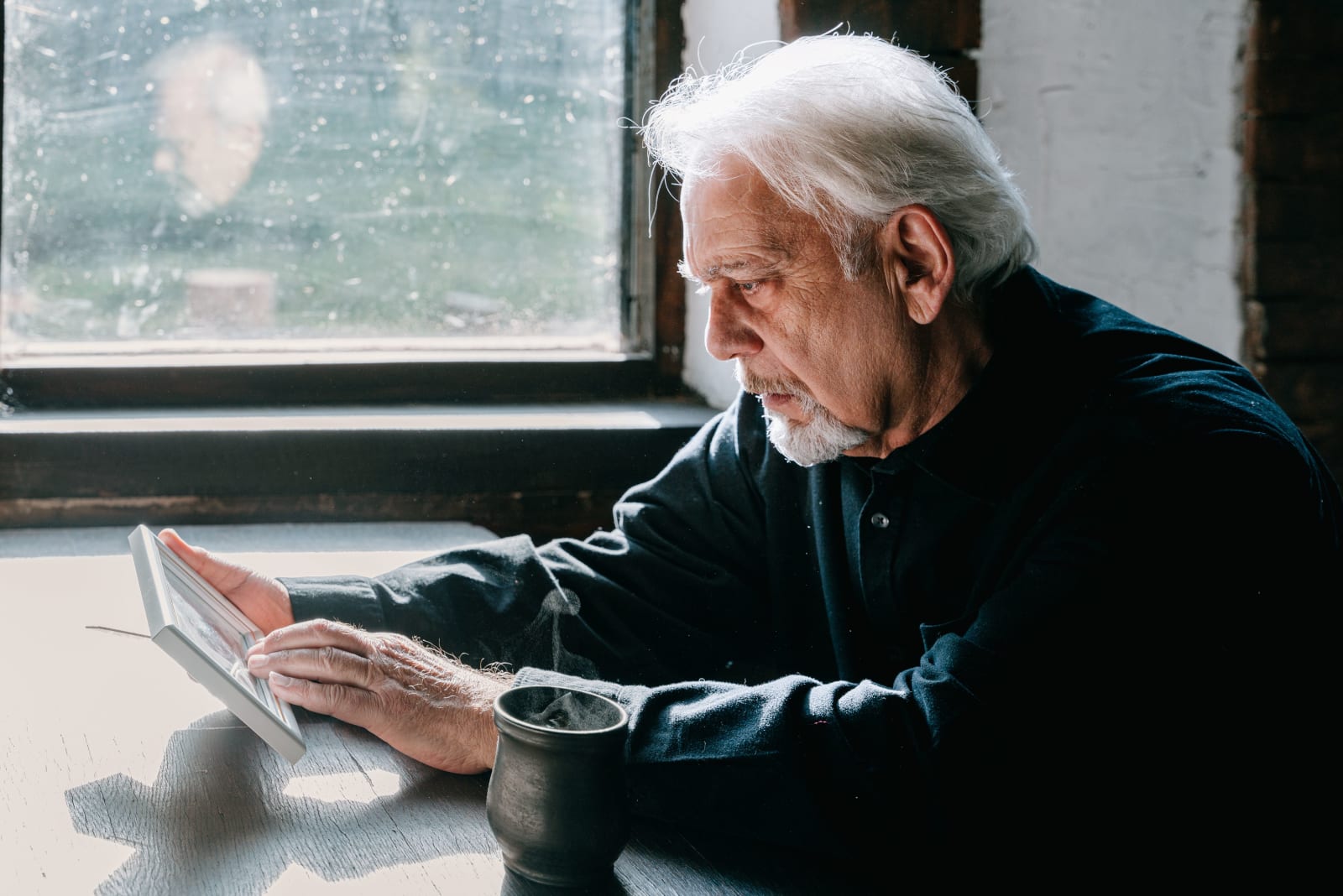 An elderly man holding a photo of a deceased loved one in grief. (Representative Image Source: Pexels| Ivan S)
