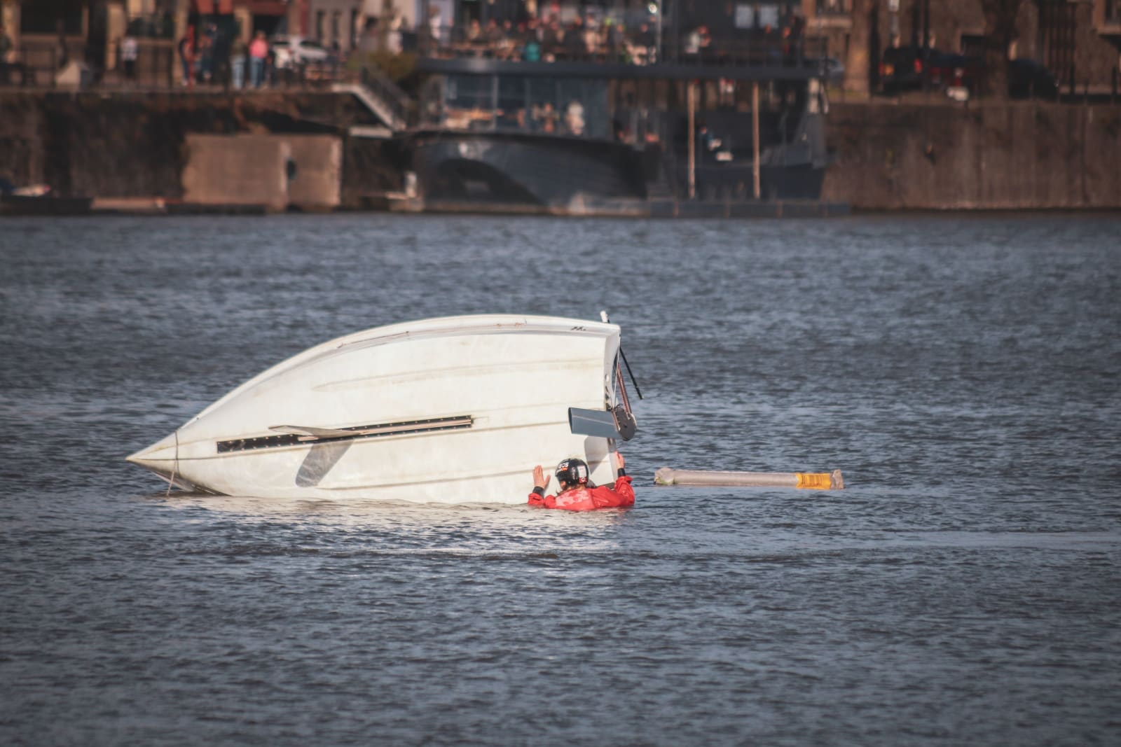 A man in life jacket near a capsized boat.