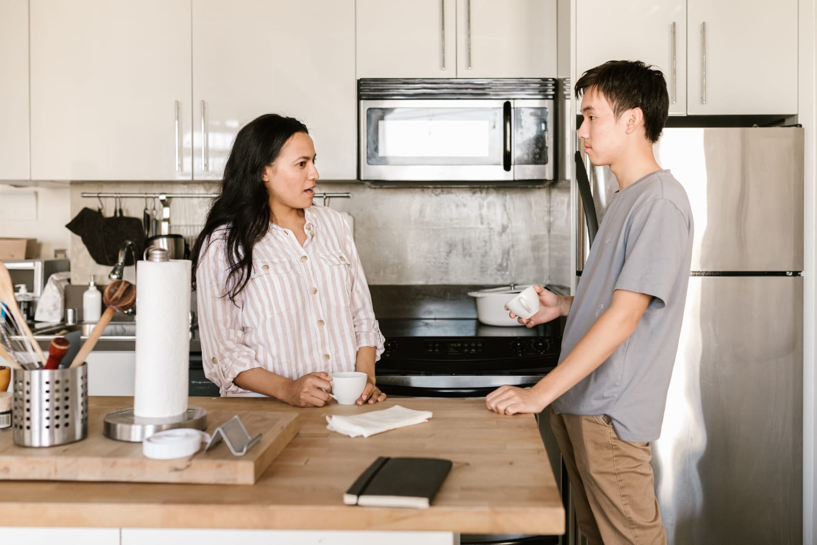 An asian man talking to a woman in kitchen.