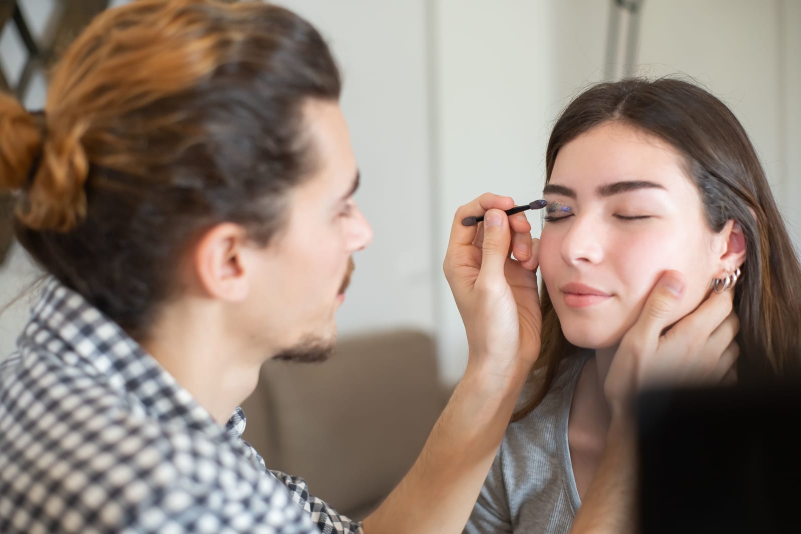 A man applying makeup on a woman's face. (Represent