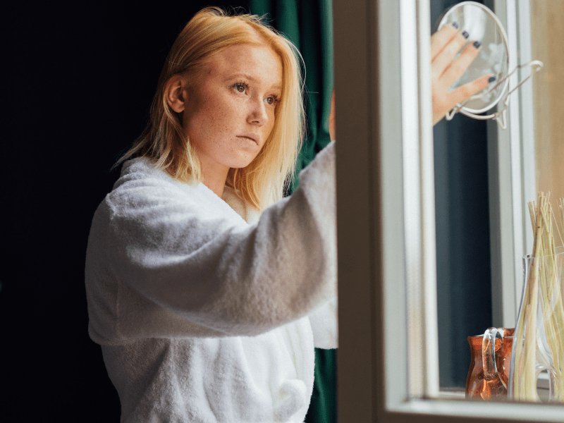 Woman looking in the mirror feeling insecure about her skin.