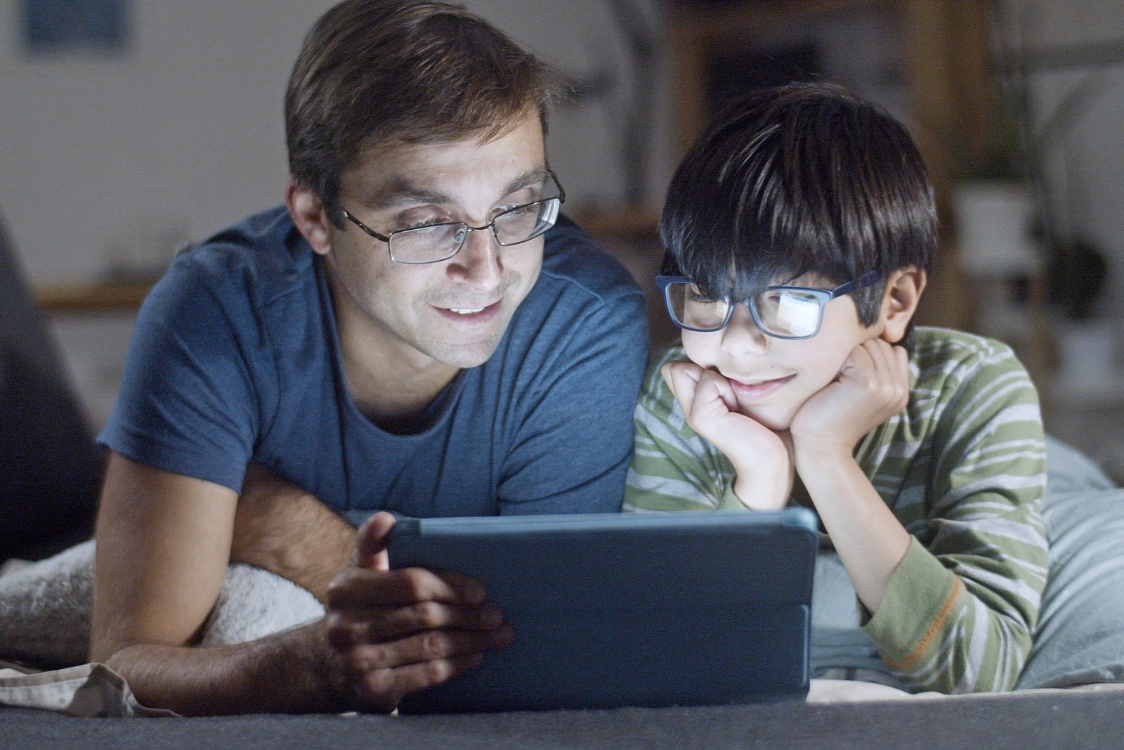 A father and son lying in bed, happily watching a tablet  (Representative Image Source: Pexels | Kampus Production)