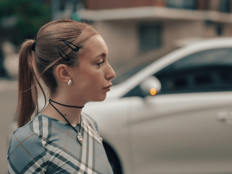 A teenage girl looking annoyed while waiting in the parking lot.